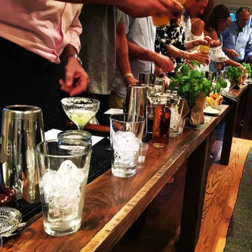 Guests lined up along a wooden bar with shaker tins, ice and fresh herbs at their workstations