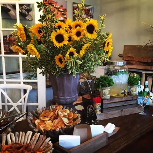 A party table with a big sunflower arrangement, a drink dispenser and snacks