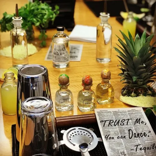 A tequila tasting station with mini bottles, a shaker, a strainer and a pineapple